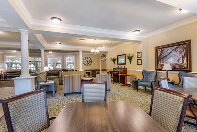 Spacious senior living common area with tables, chairs, lounge seating, decorative columns, and framed artwork.