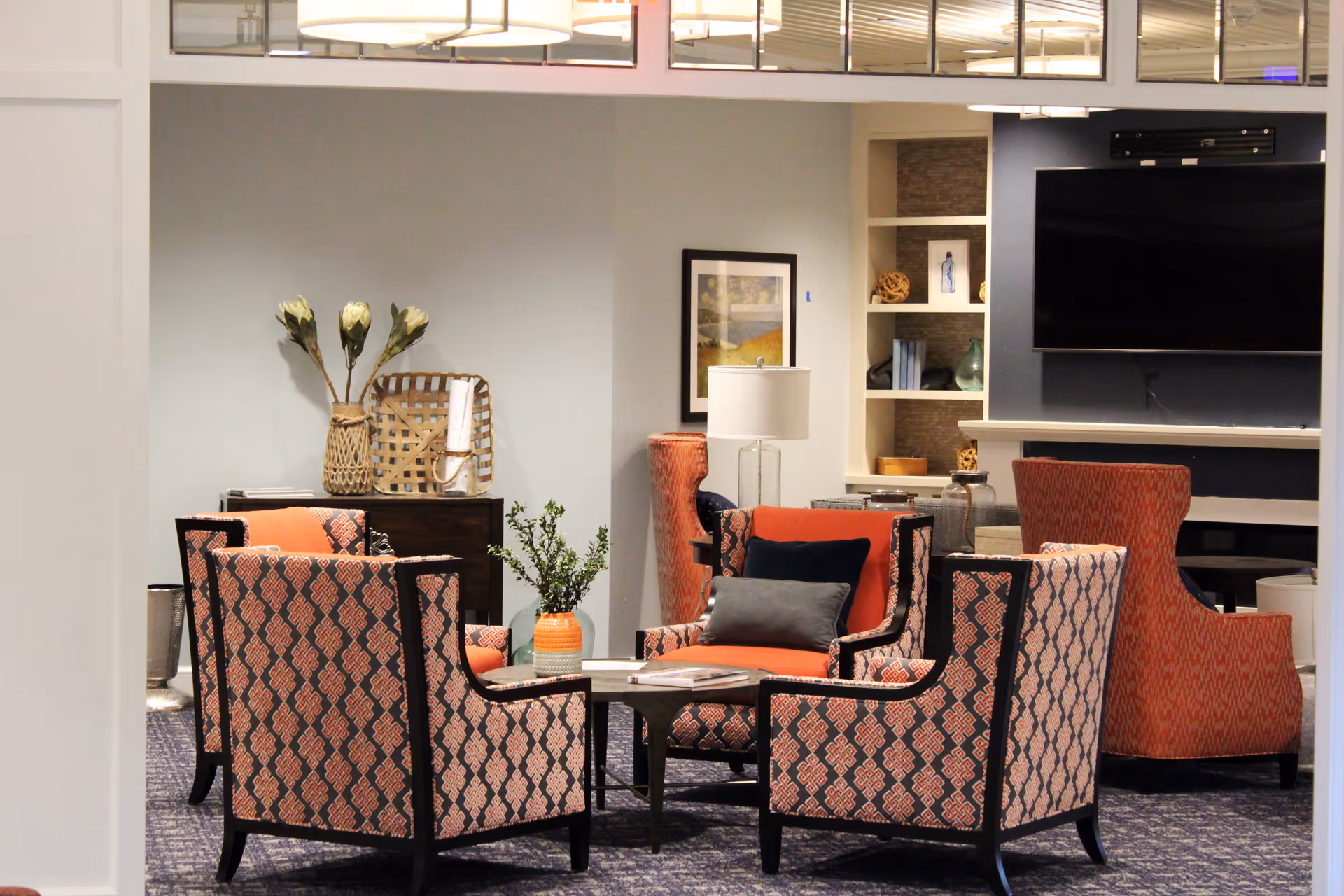 A cozy lounge area with patterned armchairs and a coffee table facing a wall-mounted TV and built-in shelving.