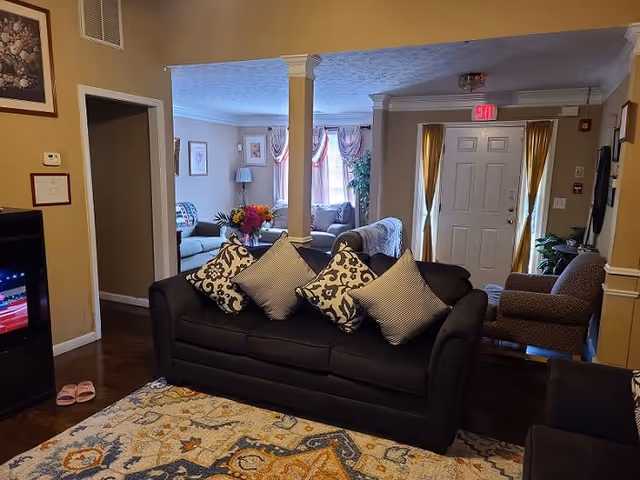 Cozy interior living room with a dark sofa topped with patterned pillows, area rug, additional seating, decorative columns, and a front door with an exit sign.