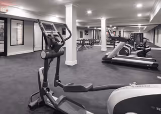 Interior fitness center with treadmills, ellipticals, weight benches, and dumbbells in a spacious, well-lit room.