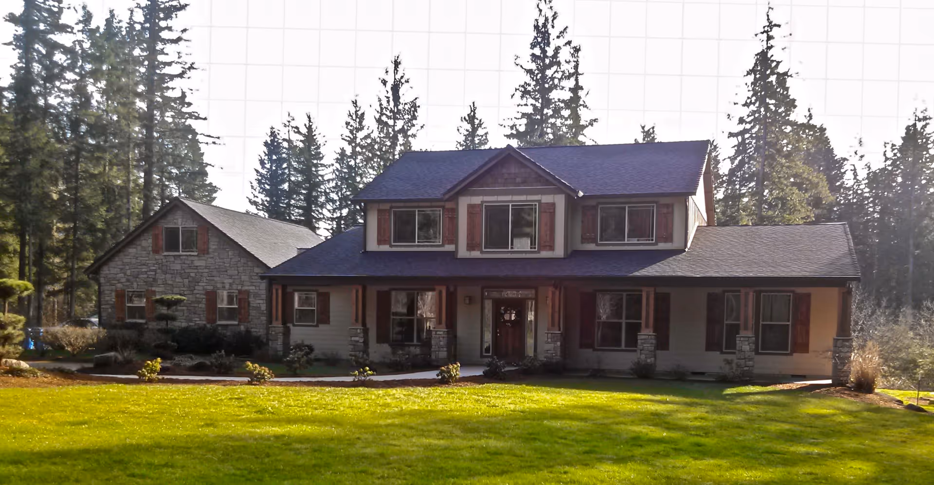 Two-story house with a large front porch, stone accents, and a green lawn surrounded by trees.