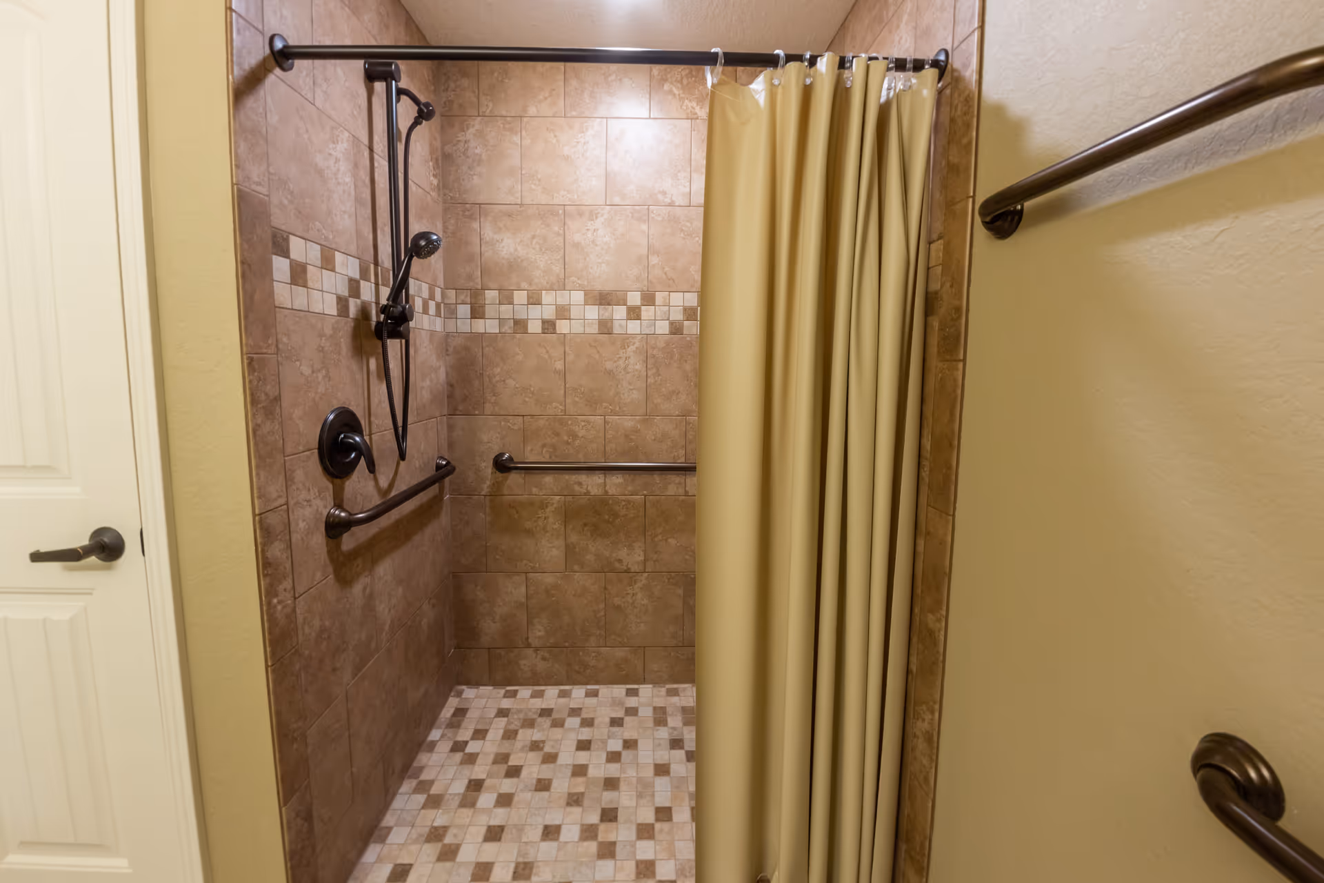 Tiled walk-in shower with grab bars, a handheld showerhead, and a beige shower curtain.