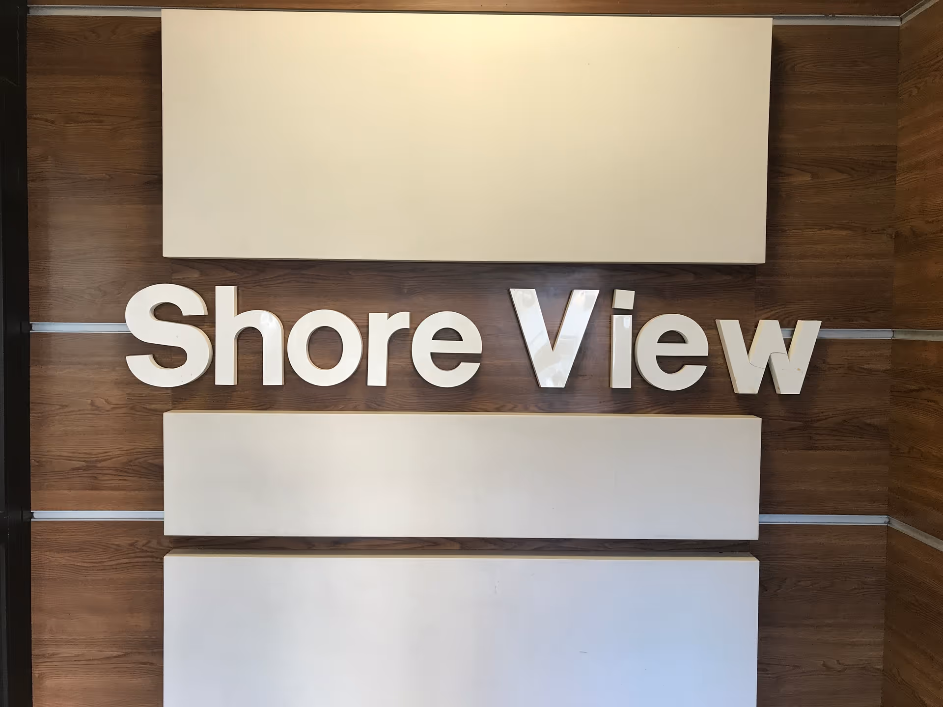 A wooden wall with three horizontal white panels and large white letters spelling 'Shore View' mounted on the middle panel.