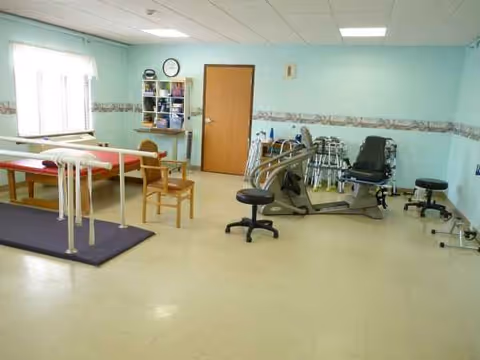 An interior therapy room with exercise equipment, parallel bars, and chairs.