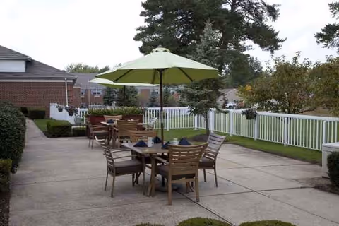 Outdoor patio with a wooden table, chairs, and a large umbrella, surrounded by a white fence.