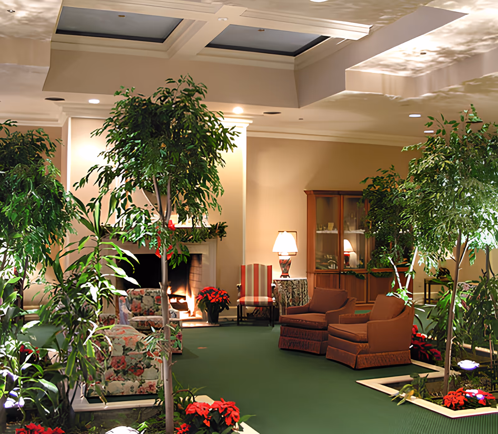 Cozy indoor lounge with armchairs, abundant potted plants, a fireplace, and poinsettia accents.