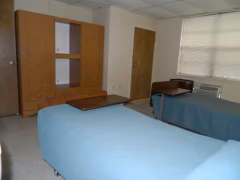 Two blue-covered beds and wooden furniture in a small shared bedroom.