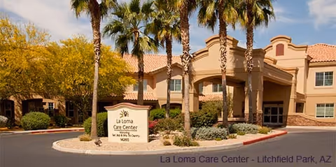 Exterior view of La Loma Care Center building with palm trees and desert landscaping in front. The building has a beige facade with a covered entrance and a sign that reads 'La Loma Care Center, Skilled Nursing & Therapy, M260'.
