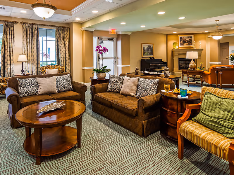 A well-appointed common lounge with sofas, armchairs, coffee tables, a piano, and a fireplace.