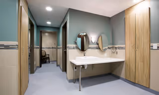 Accessible bathroom area with a wall-mounted sink, two round mirrors and sconces, wooden doors, and a hallway leading to additional rooms.
