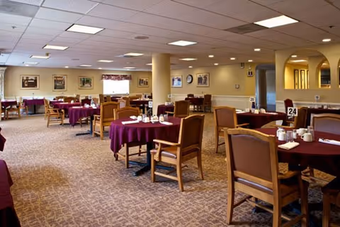 Spacious senior dining room with round tables covered in purple tablecloths and wooden chairs.