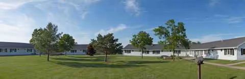 Long, single-story facility with a white and blue exterior, green lawn, and several trees.