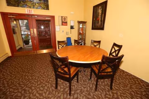 Round wooden table with six chairs in a beige dining area near double doors.
