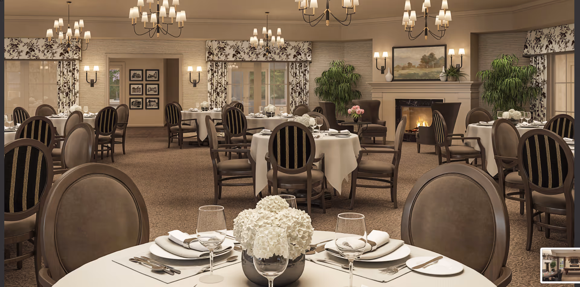 Elegant dining room with round tables covered in white tablecloths, set with plates, napkins, cutlery, and wine glasses. The room features upholstered chairs, floral curtains, multiple chandeliers, wall sconces, a fireplace with a painting above it, and potted plants.