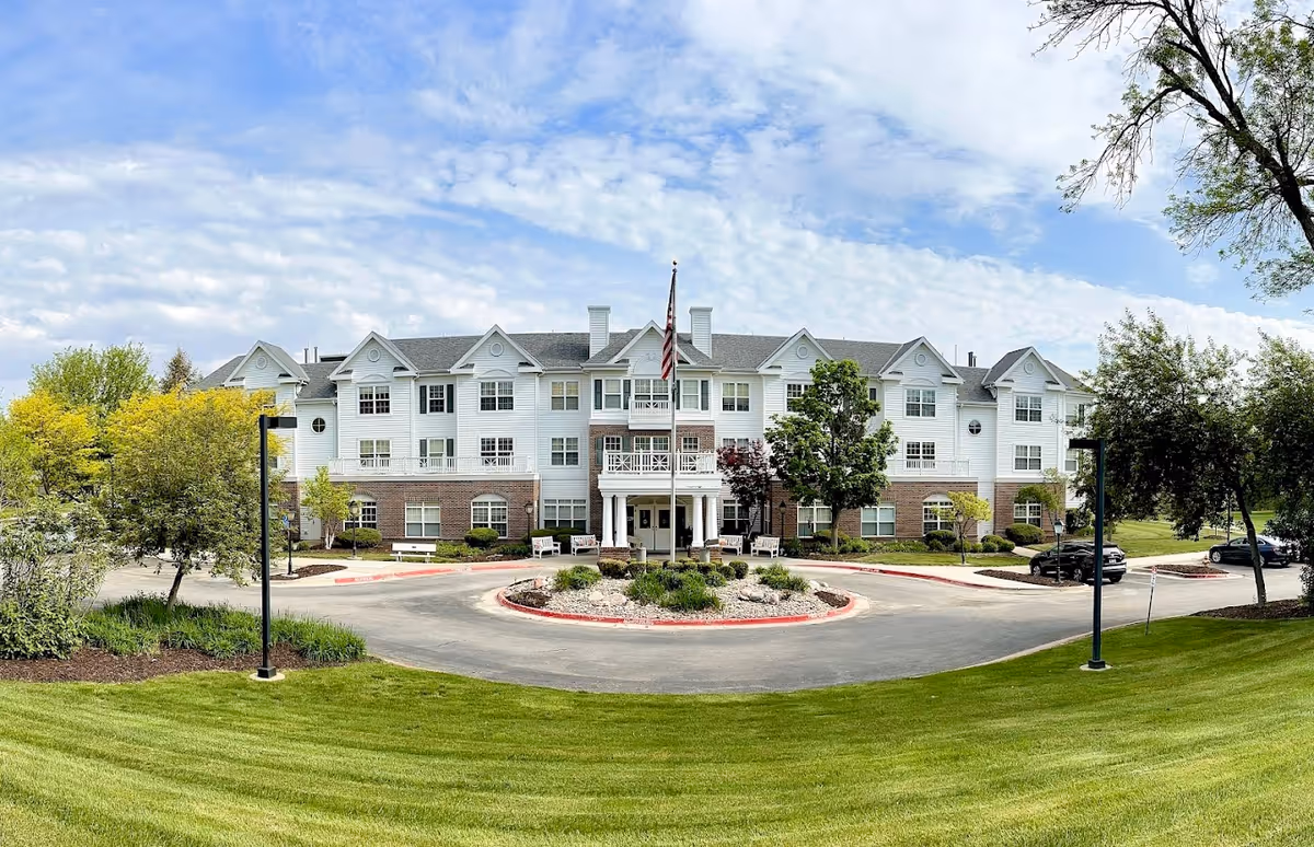 Front view of a large white senior living building with circular driveway and landscaping.