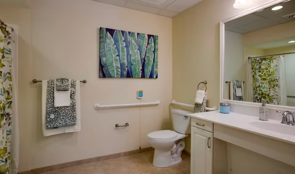 Accessible bathroom with a toilet, grab bars, sink and vanity with mirror, patterned towels and shower curtain, and botanical wall art.