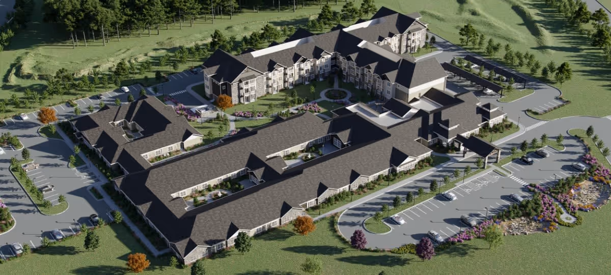 Aerial view of The Crestone Senior Living facility showing multiple connected buildings with dark roofs, surrounded by landscaped greenery, parking lots with cars, and walking paths.