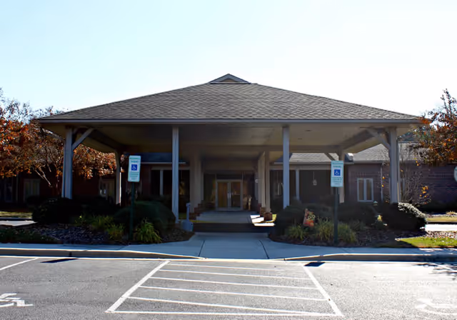 Covered porte-cochère entrance of a single-story brick senior living facility with accessible parking in front.