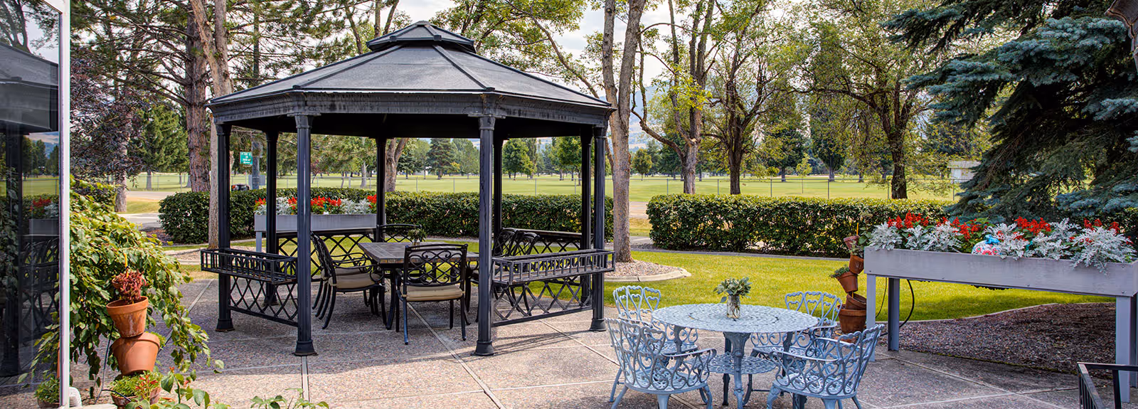 Outdoor patio area with a black metal gazebo, multiple seating tables, planters, and lawn beyond.