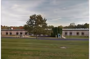 Exterior view of a single-story building with a grassy lawn and central tree.