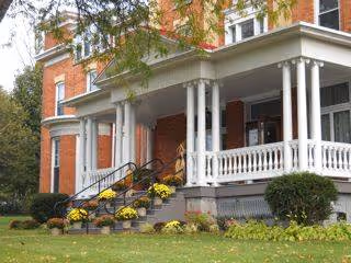 Front view of a brick senior living home with a white porch, stairs, and landscaping.