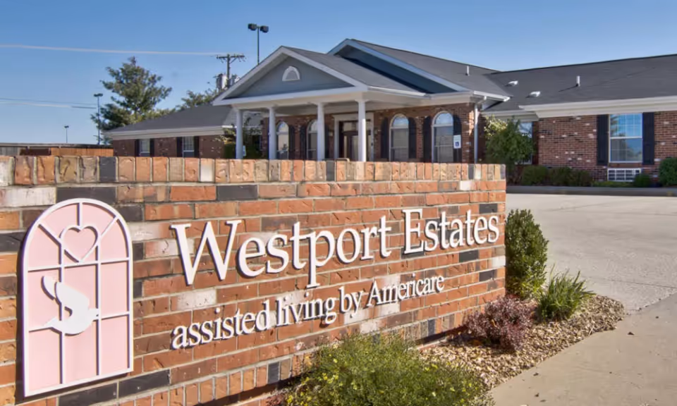 Brick sign reading Westport Estates assisted living by Americare in front of a single-story brick senior living building.