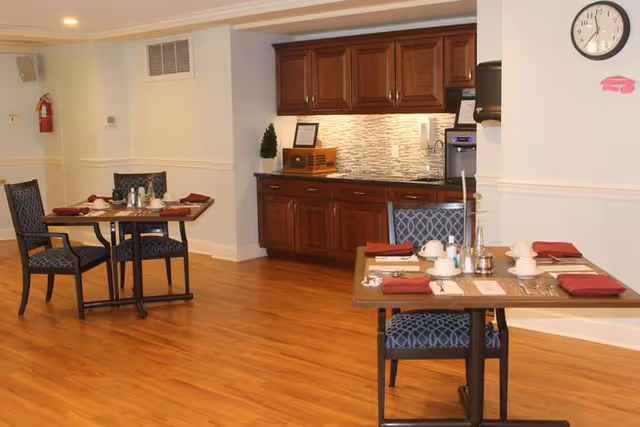 Dining area with two tables set for meals, wood floors, and a kitchenette against the wall.