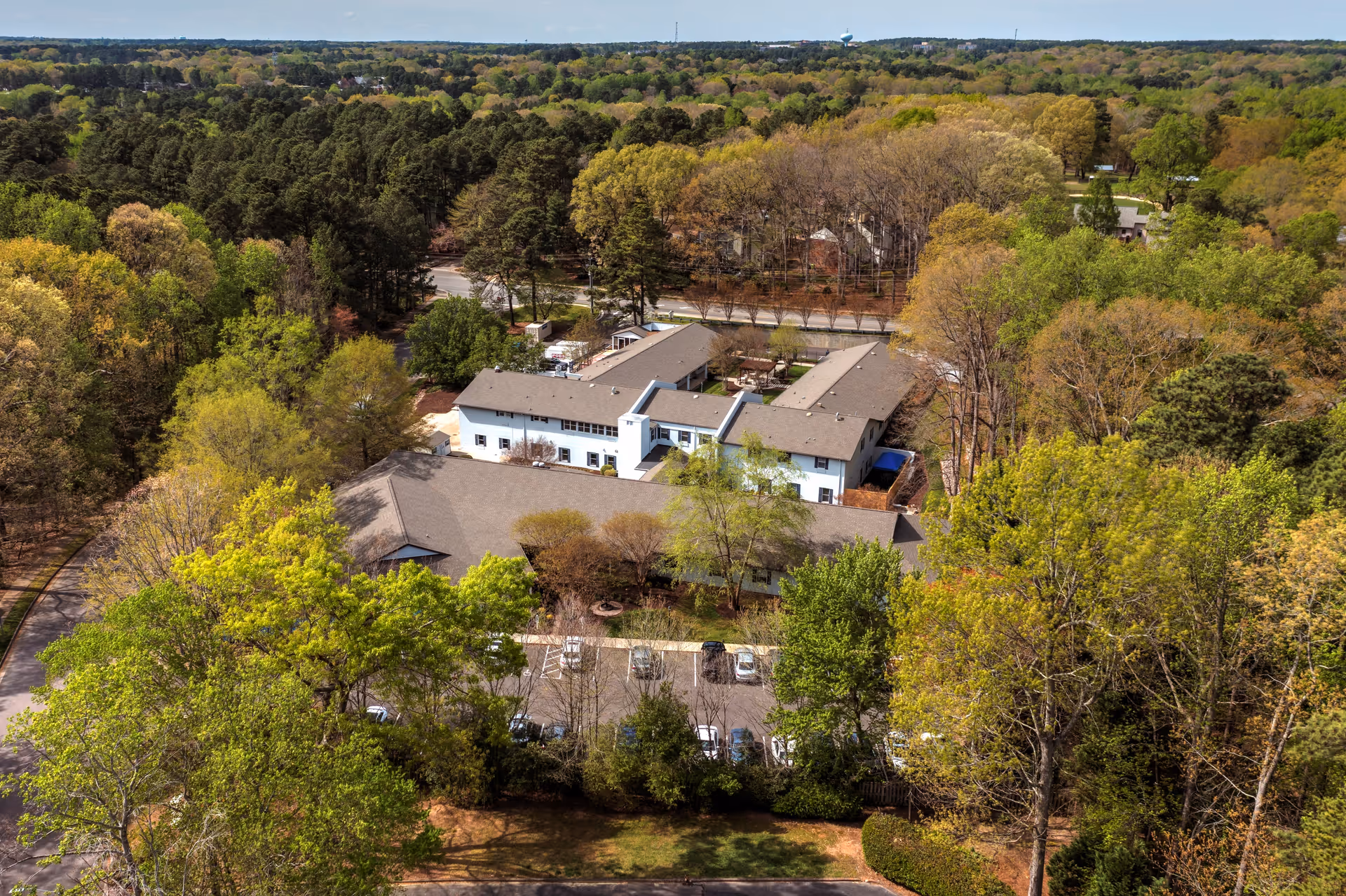 Aerial view of TerraBella Northridge senior living facility surrounded by dense green trees and foliage, with a parking lot visible in front of the building.