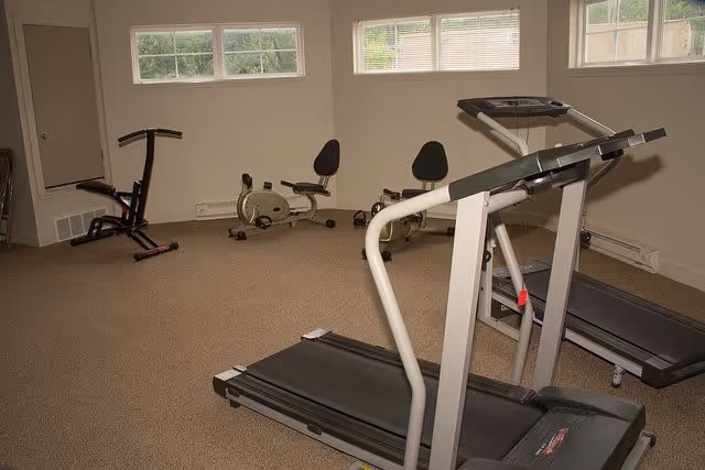 Small fitness room with two treadmills, two recumbent bikes and other exercise equipment under high windows.