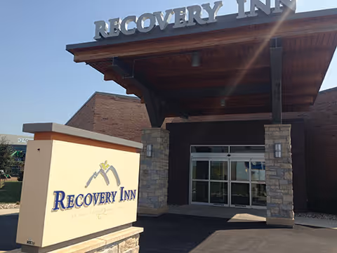 The entryway of Recovery Inn showing a covered portico, glass doors, and a freestanding sign with the facility name.