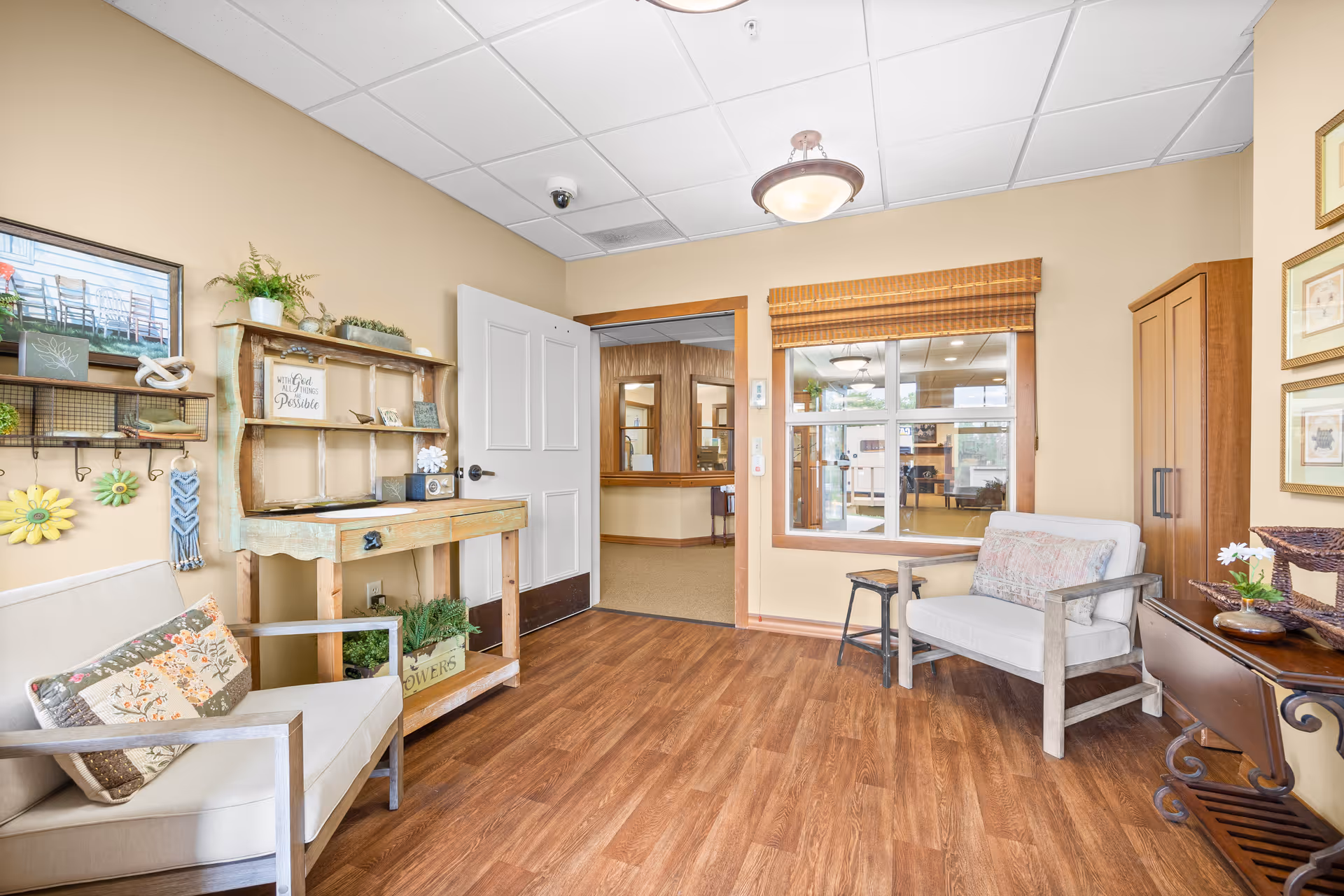 Small reception-style sitting area with two upholstered chairs, rustic shelving, and a window into an adjacent hallway.