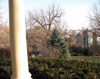 View from a porch with a column, leafless trees, and distant houses.