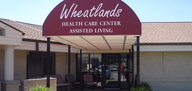 Front entrance of Wheatlands Health Care Center assisted living with a maroon canopy sign over the doorway.