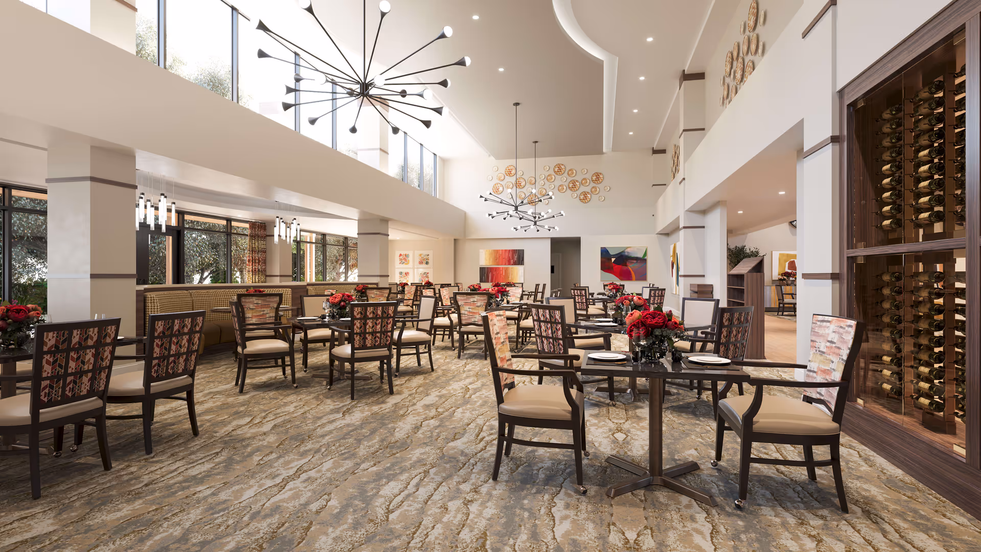 A spacious, well-lit dining room with multiple tables and chairs arranged neatly. Each table has a centerpiece of red flowers. The room features large windows allowing natural light, modern chandeliers, decorative wall art, and a wine rack on the right side.