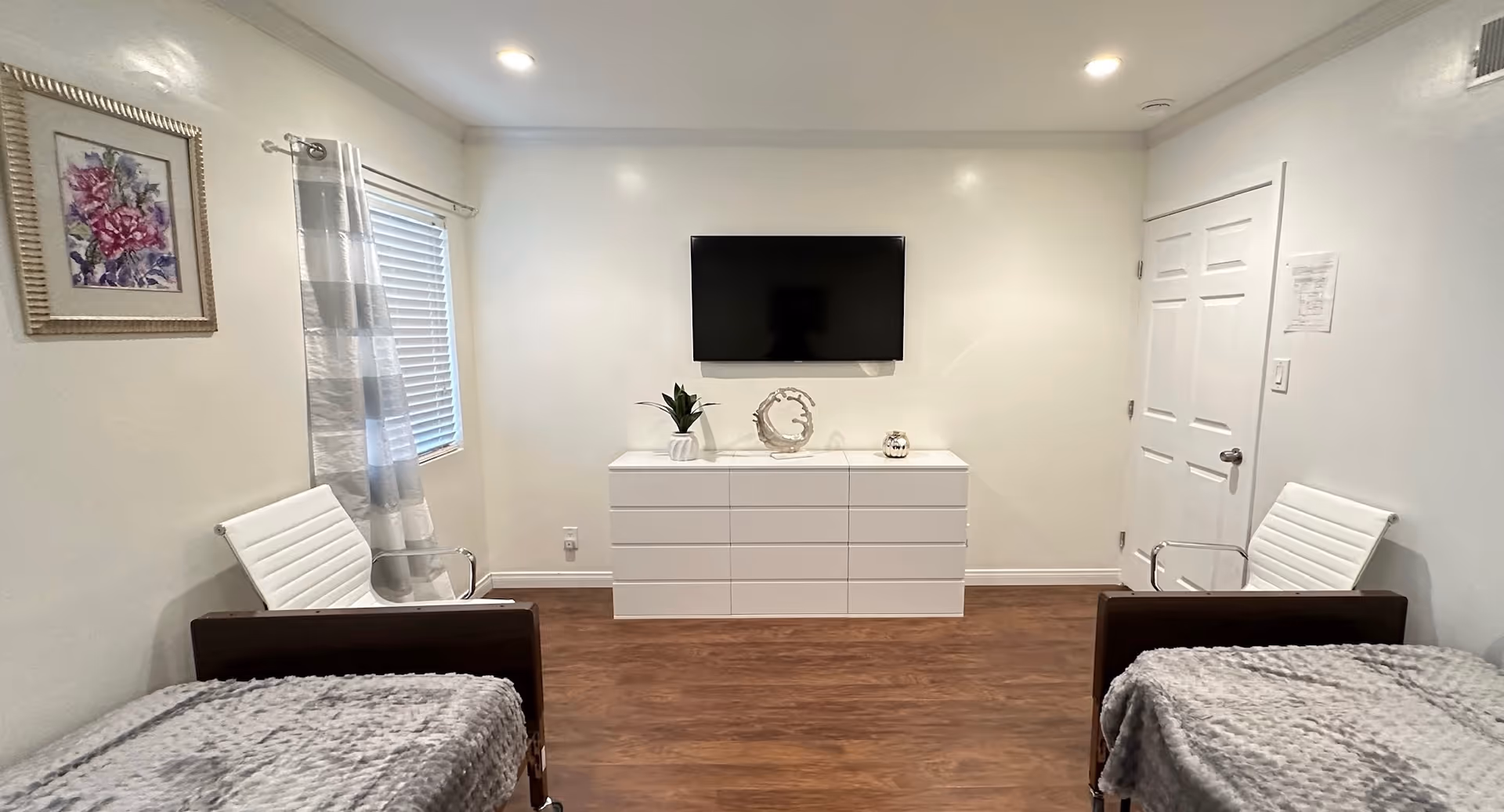 Two twin beds and a dresser with a wall-mounted TV in a bright, minimalist bedroom.