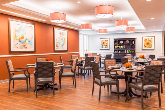 Dining room with round tables and chairs, pendant lights, framed artwork, and table settings.