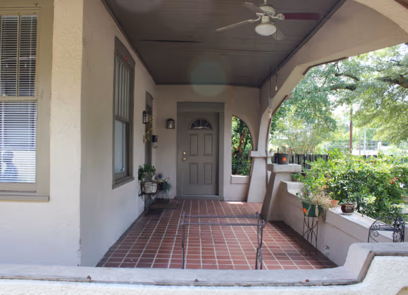 Covered front porch with tiled floor, arched openings, potted plants, and a gray entry door.
