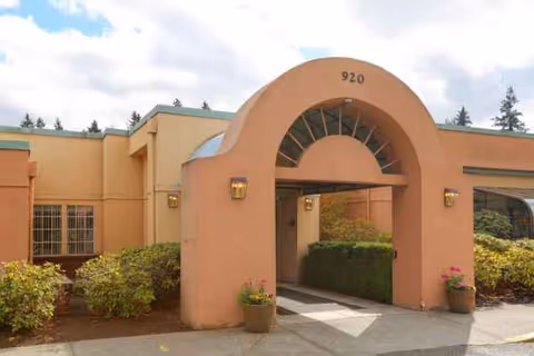 Peach-colored building entrance arch with walkway and shrubs in front.