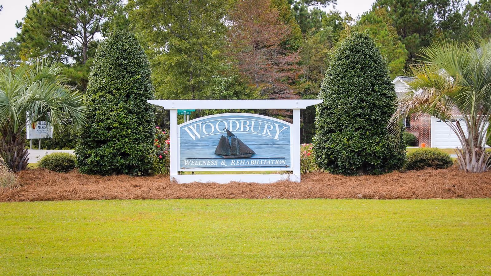 Entrance sign reading 'Woodbury Wellness & Rehabilitation' on a landscaped lawn with shrubs and trees.