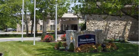 Stonebrooke Rehabilitation Center exterior with stone wall, sign, and landscaping.