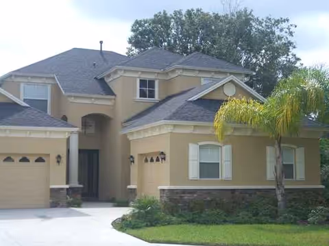 Beige two-story building with a driveway, entrance, and palm tree in front.