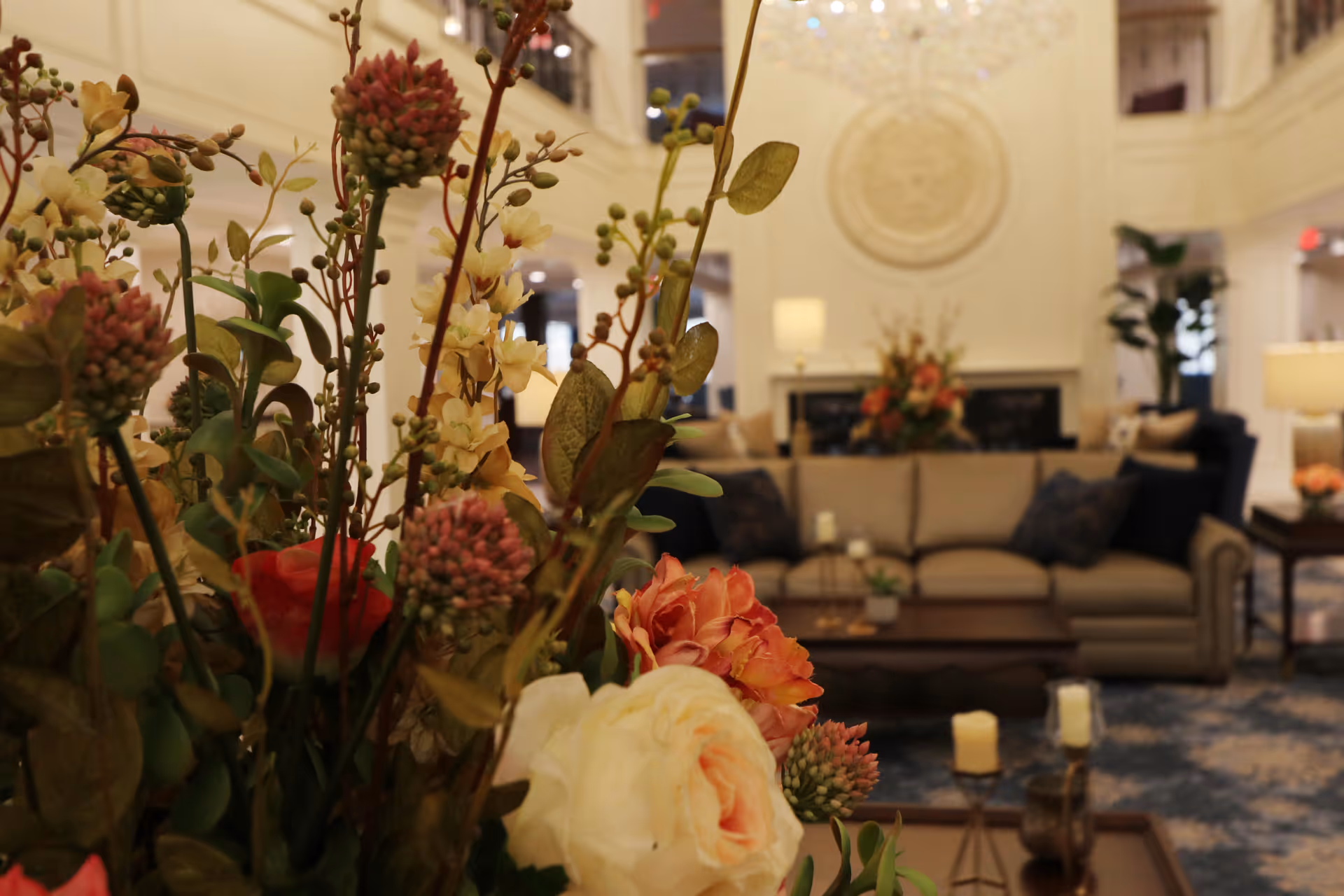 Close-up floral arrangement in the foreground with a plush seating lounge and fireplace in the background of a senior living facility lobby.