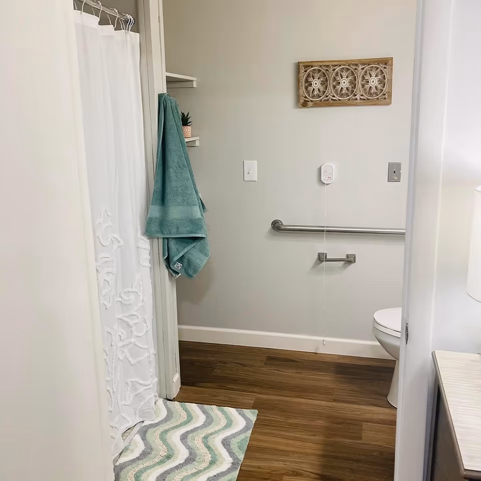 Accessible bathroom interior with a shower curtain, teal towel and rug, wall grab bar and a partially visible toilet.