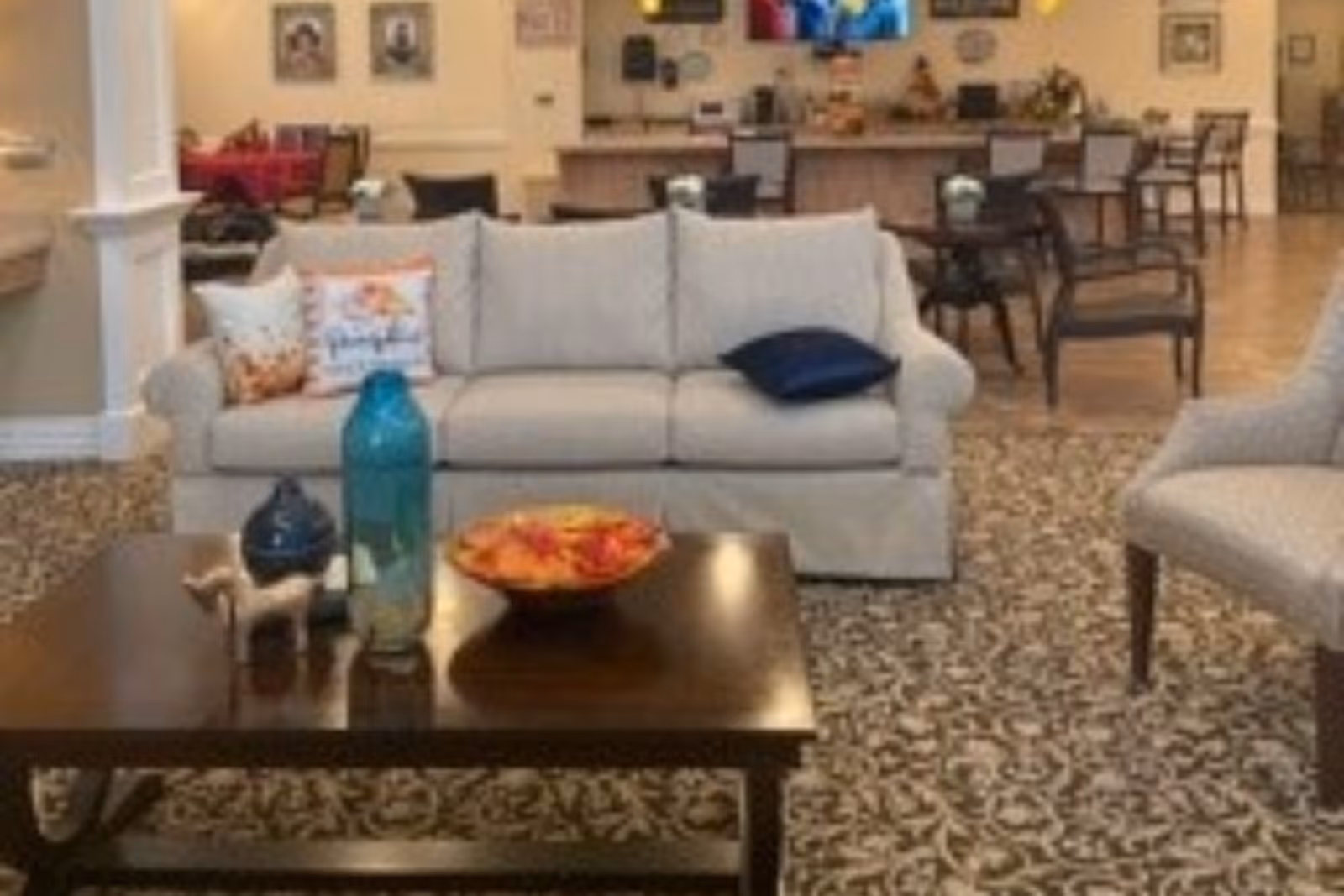 Lounge-style seating area featuring a beige sofa, a coffee table with decorative items, and dining tables in the background.