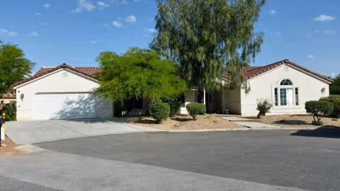 A single-story retirement home with a white exterior, red-tiled roof, and desert landscaping.
