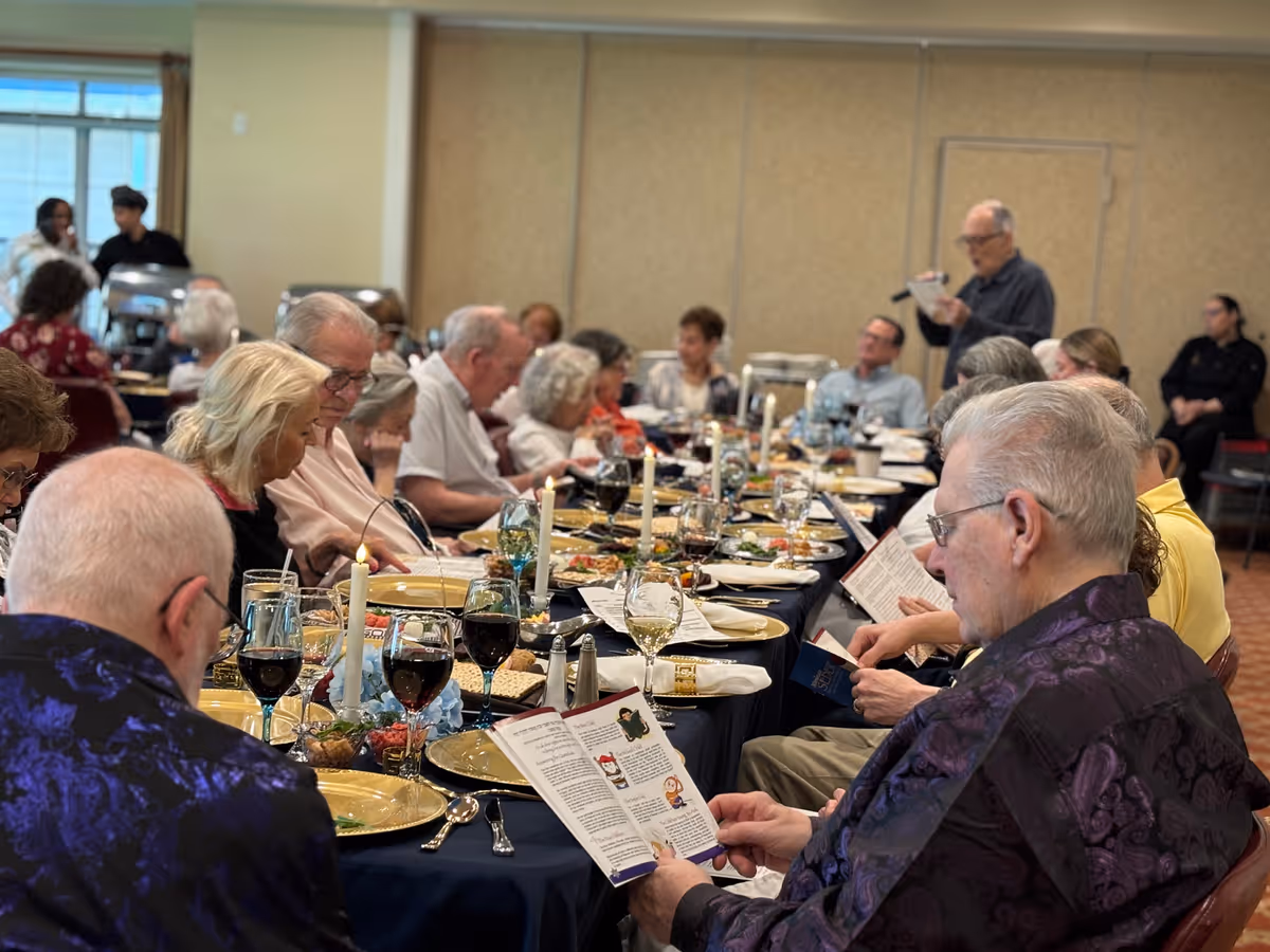 Elderly residents seated around a long, candlelit dining table sharing a communal meal in a senior living facility.