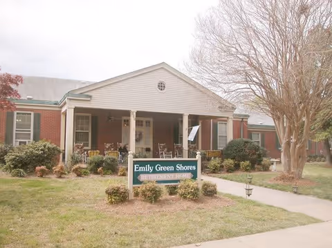 Front entrance of a brick retirement home with a covered porch and a sign reading "Emily Green Shores".