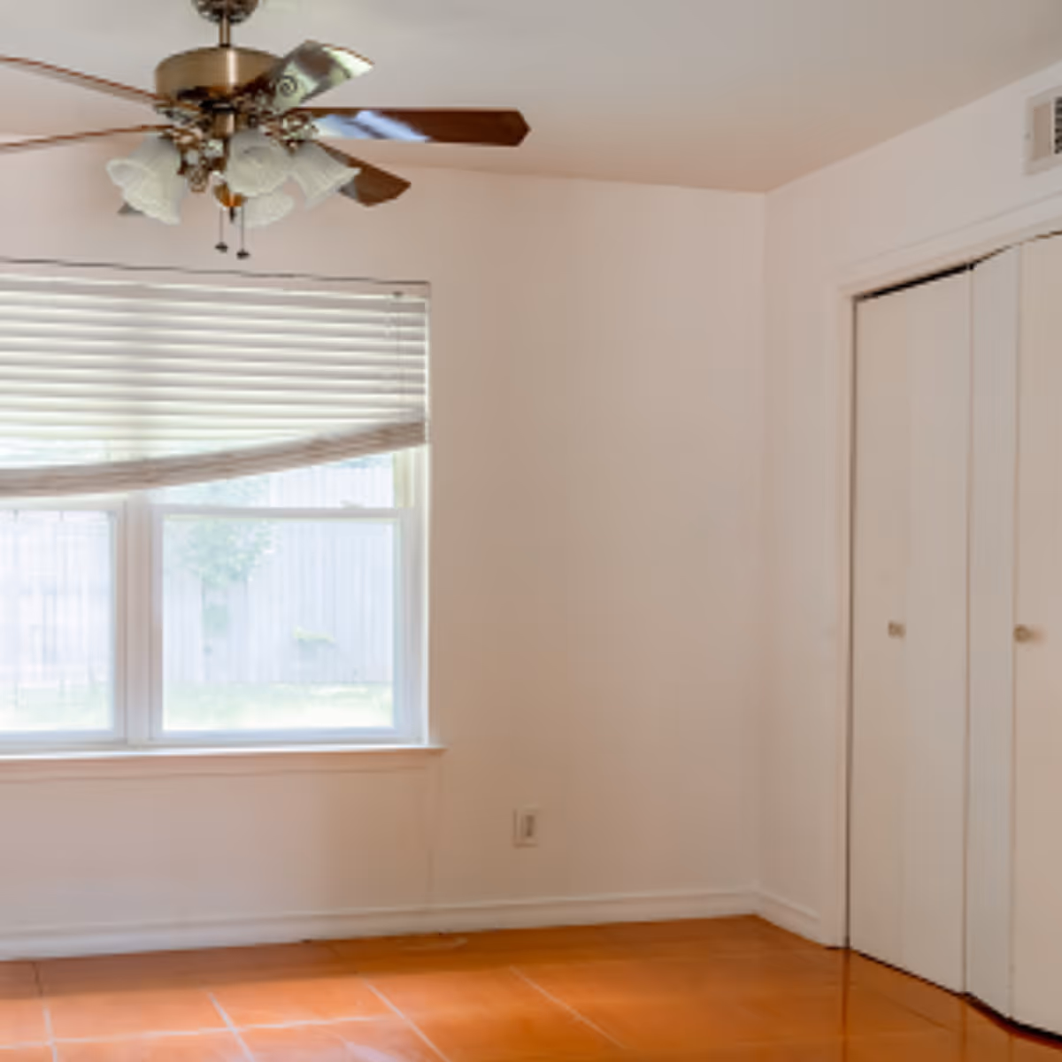 Empty room with a ceiling fan, window with blinds, closet doors, and a hardwood floor.