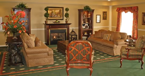 Well-appointed living room with sofas and armchairs arranged around a fireplace and coffee table, with decorative plants and framed art.