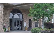 Front entrance of a brick healthcare facility with arched glass doors, potted plants, and a covered portico.